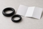 Two generic black ring-shaped accessories beside a blank folded leaflet, unused on a neutral surface.