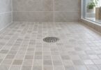 Round stainless-steel shower drain grate set in a tiled shower floor.