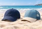 Two generic unbranded baseball and mesh-back caps on sand beside the ocean.