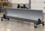 Illustration of a detached snowplow blade resting on wheeled supports in a garage.
