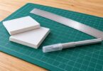 Paper-faced foam board, a metal ruler and a capped craft knife on a cutting mat.