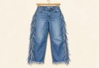 Illustration of blue jeans with fringed outer seams and hems on a hanger.