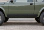 A flat black rocker-panel cover mounted flush below the door of a generic older two-door off-road vehicle.