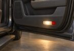 Illustration of a courtesy lamp in the lower interior panel of an open SUV door.