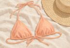 Illustration of a generic peach triangle bikini top on cream fabric beside a straw hat.