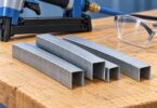 Generic metal staple strips beside a pneumatic stapler and safety glasses.
