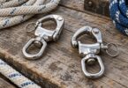 Two generic stainless steel swivel-eye snap shackles beside rope on a wooden surface.