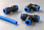 Detached straight, elbow and tee tube fittings with blue release collars beside a separate length of blue tubing.