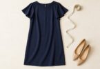 Generic navy flutter-sleeve shift dress beside a measuring tape and shoes.