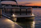 A stationary generic pontoon boat beside a dock at dusk with low docking lights.