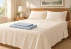 Cream sheets and pillows with folded blue bedding on a queen-size bed.