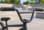 Generic BMX handlebar with ribbed black grips and covered bar ends near a skatepark.
