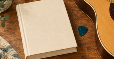 Illustration of a closed plain music-reference book beside a guitar pick and the edge of an acoustic guitar.