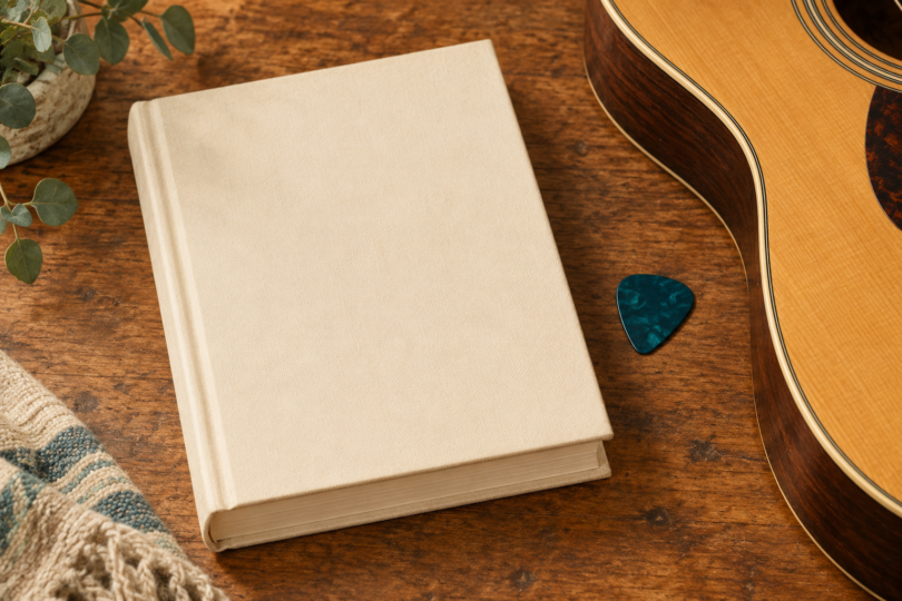 Illustration of a closed plain music-reference book beside a guitar pick and the edge of an acoustic guitar.