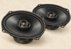 Illustration of two plain oval automotive speakers on a neutral surface.