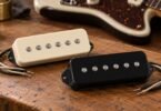 Ivory and black wide single-coil guitar pickups with six pole pieces each on a wooden workbench.