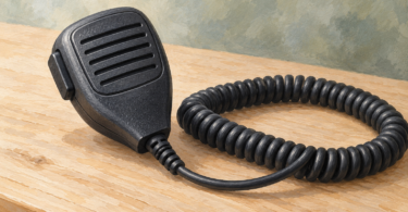 Handheld radio microphone with a coiled cord on a desk.