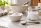 White powder in a bowl, glass jar and measuring spoon on a kitchen counter.