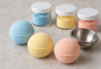 Blue, yellow and peach bath bombs beside closed jars of colored powder and a metal bath-bomb mold.