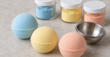 Blue, yellow and peach bath bombs beside closed jars of colored powder and a metal bath-bomb mold.