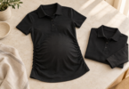 A black short-sleeve polo with side ruching beside a folded black long-sleeve polo on a pale tabletop.