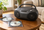 A dark portable CD boombox with a raised handle sits on a wooden table beside two compact discs in open cases.