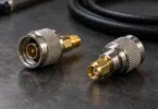 Two generic metal coaxial adapters beside a black cable on a dark workbench