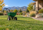 An unbranded push spreader on a lawn beside a gravel garden border, with foothills in the distance.