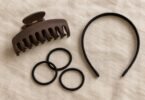 Generic brown claw clip, black headband and three black hair elastics arranged on beige linen