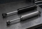 Illustration of two unbranded pickup-truck shock absorbers on a gray workbench.