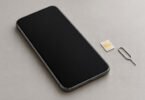Generic unbranded smartphone with a blank screen beside a SIM card and eject tool on a desk