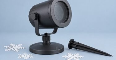 Illustration of an unbranded dark projector on a round base beside a garden stake and paper snowflakes