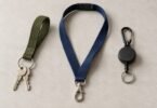 Illustration of an olive wrist key loop, navy neck lanyard and black retractable key reel arranged on a light tabletop.