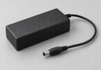 Generic black power adapter with a disconnected barrel plug on a gray surface.
