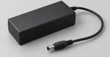 Generic black power adapter with a disconnected barrel plug on a gray surface.