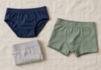 Illustration of flat lay of unbranded navy briefs, sage-green boxer briefs and a folded gray pair on a neutral fabric surface.