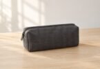 Illustrative image of a closed, unbranded gray accessory pouch on a plain wooden table.