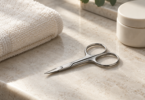 Illustration of closed stainless-steel cuticle scissors beside an ivory towel and an unmarked cream jar