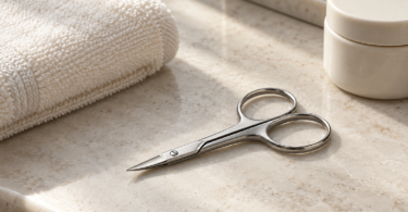 Illustration of closed stainless-steel cuticle scissors beside an ivory towel and an unmarked cream jar