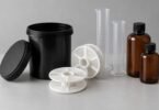 Unbranded developing tank, two empty film reels, measuring cylinders and amber bottles on a gray surface.