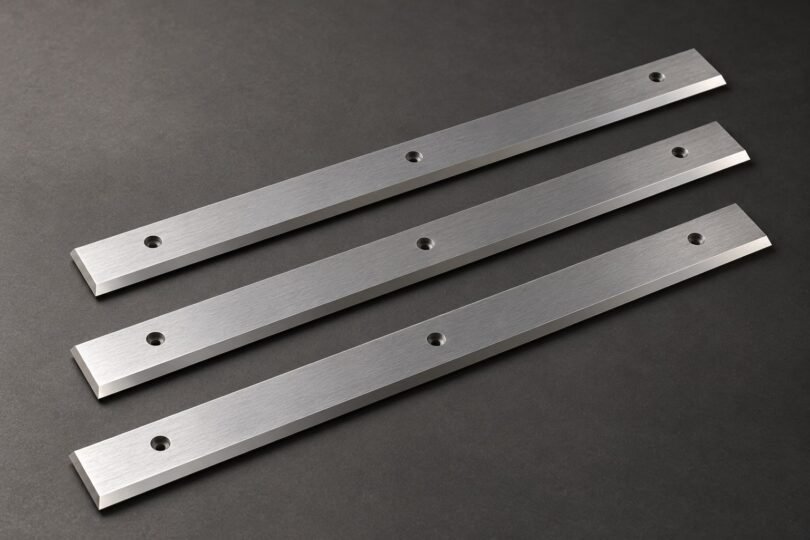 Illustration of three generic straight planer knives on a gray surface.