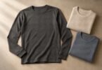 A charcoal long-sleeve crewneck top beside folded oatmeal and slate thermal tops on a neutral surface.