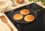Illustration of pancakes on a round griddle resting on a glass cooktop beside a wooden spatula.