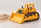 Illustration of an unbranded yellow toy bulldozer beside a small pile of sand.