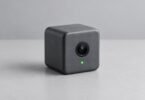 Small unbranded gray cube camera with a green indicator on a plain gray desk.
