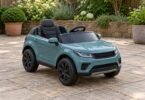 An empty teal ride-on toy car with dark tires parked on a dry garden patio.