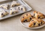Unbaked blueberry scone portions on a parchment-lined tray beside golden baked scones on a plate