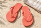 Generic coral flip-flops on pale stone beside a folded cream towel