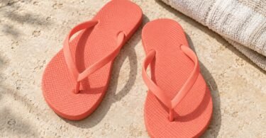 Generic coral flip-flops on pale stone beside a folded cream towel