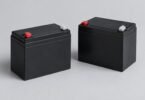 Two detached unbranded black sealed batteries with protected terminals on a gray surface
